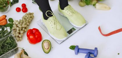 Person standing on scales surrounded by fresh produce and fitness equipment symbolizing a balanced lifestyle.