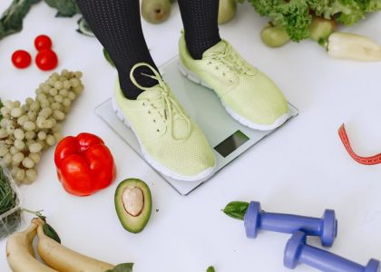 Person standing on scales surrounded by fresh produce and fitness equipment symbolizing a balanced lifestyle.